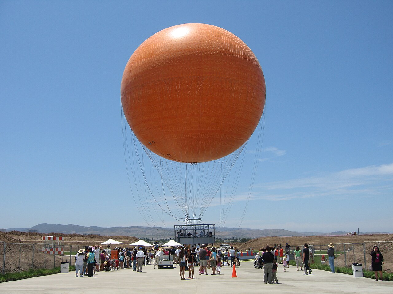 The large orange balloon above visitors and the walkway at Great Park in Irvine