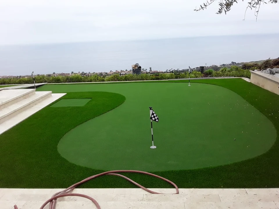 Artificial putting green with checkered flags, curved fringe turf, stone steps and an ocean view