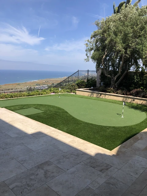 Coastal backyard putting green and stone patio