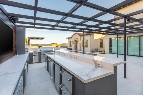 Covered outdoor kitchen island and bar beneath pergola