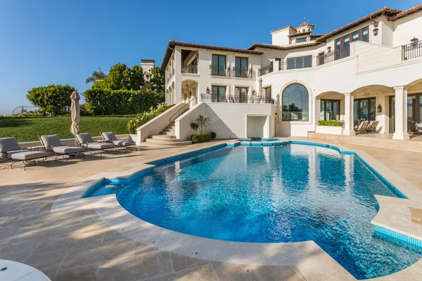 Curved swimming pool beside stone deck and residence in Pelican Hill