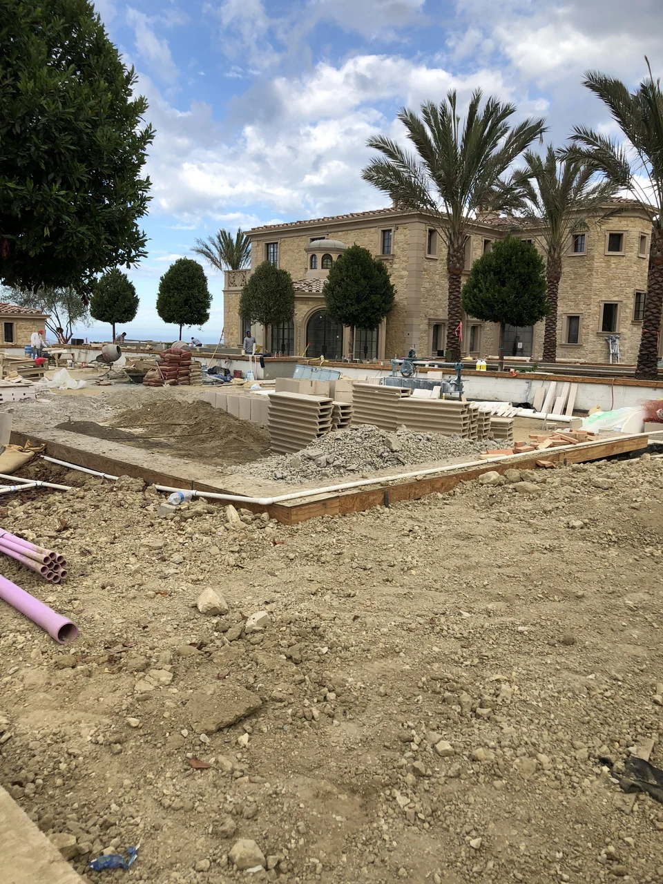 Extensive exterior construction with excavation, formwork, palms and trees around a large residence