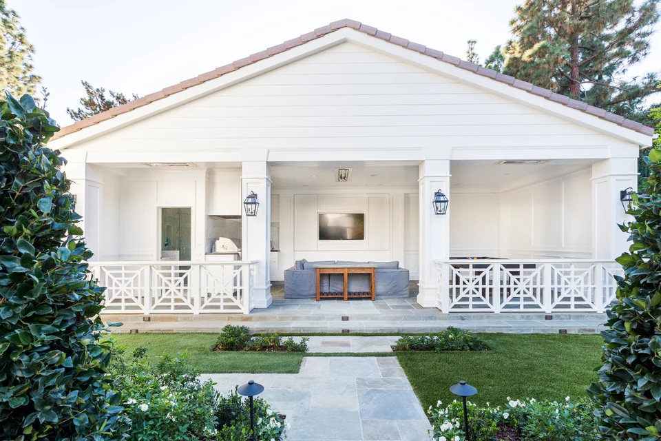 White pool house with a gabled roof, geometric railings and a garden path leading to the central entrance