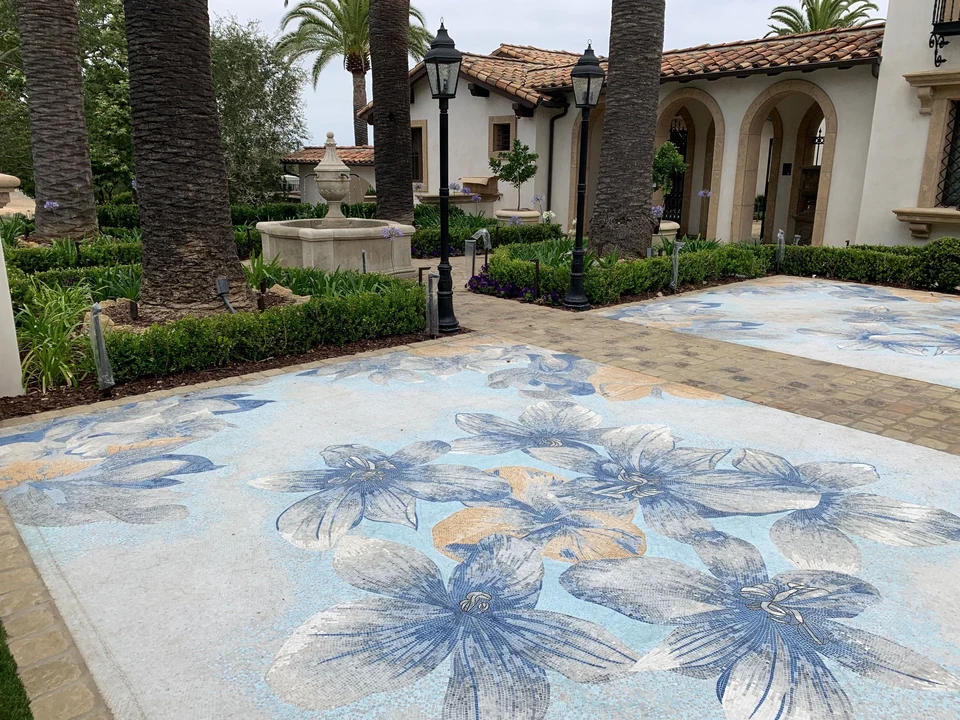 Blue, white and gold floral mosaic tile paving framed by stone in a landscaped courtyard