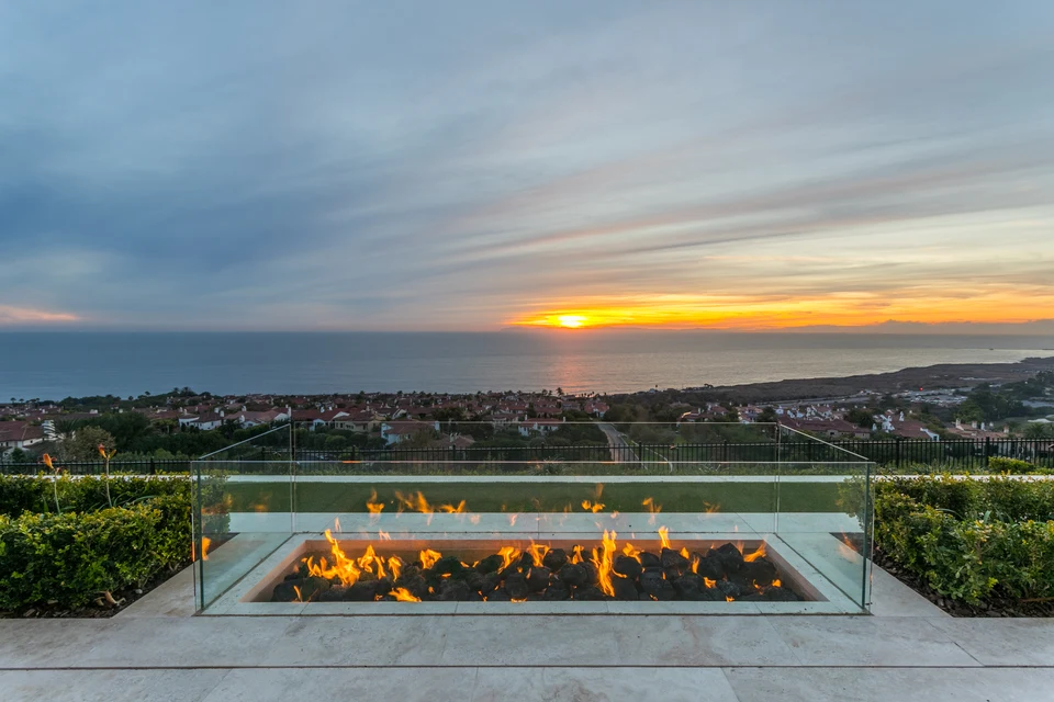 Lit rectangular fire feature with a glass surround on an ocean-view terrace at sunset