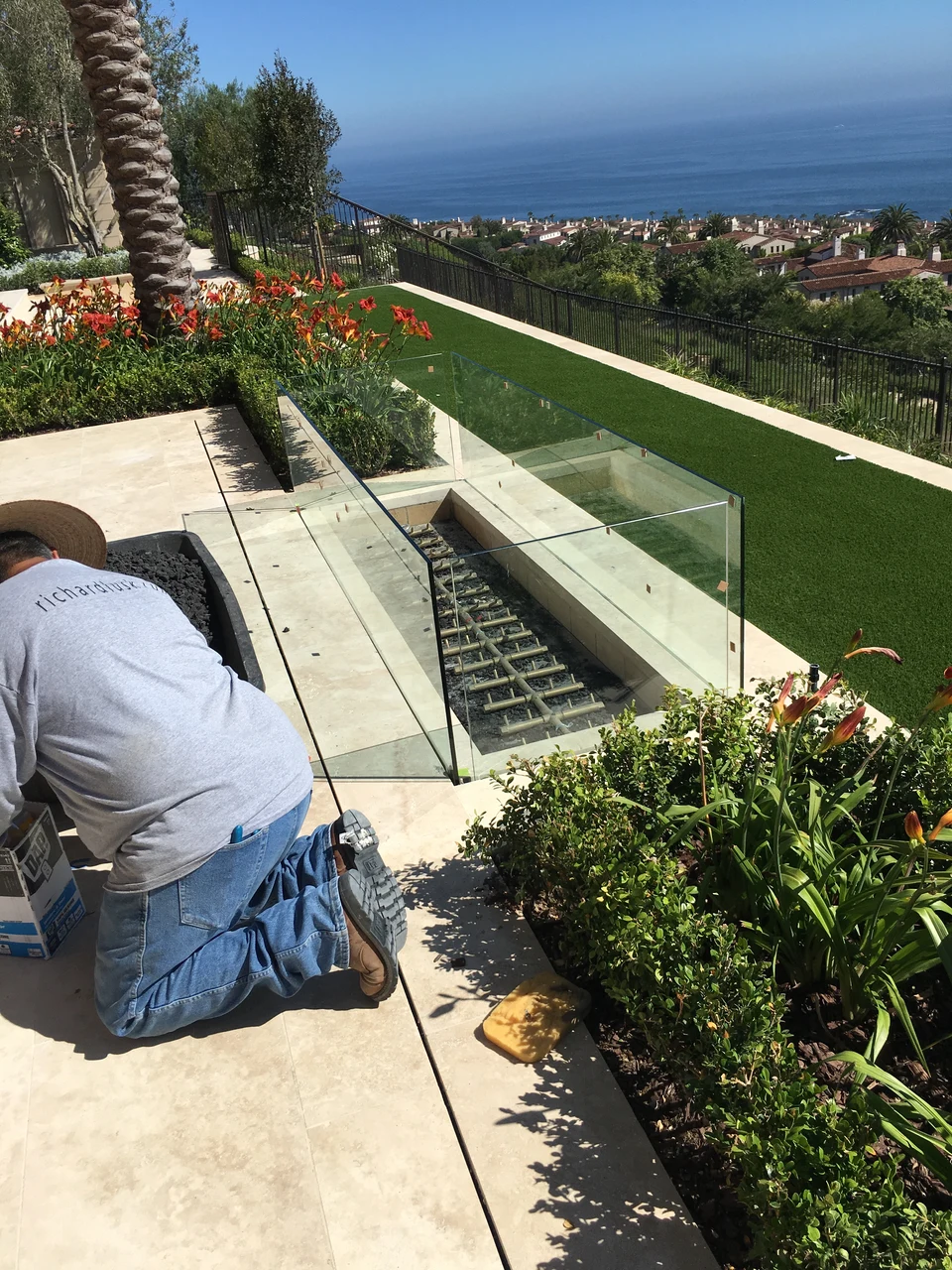 Crew member working beside a recessed linear fire feature with glass panels on a coastal terrace