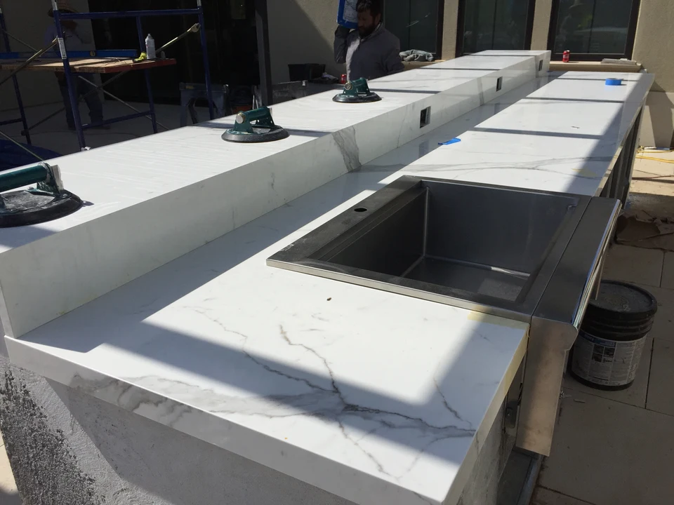 Workers fitting veined countertop pieces around a sink opening and raised outdoor bar