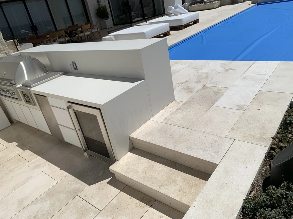 Paving and broad steps beside an outdoor kitchen and covered pool