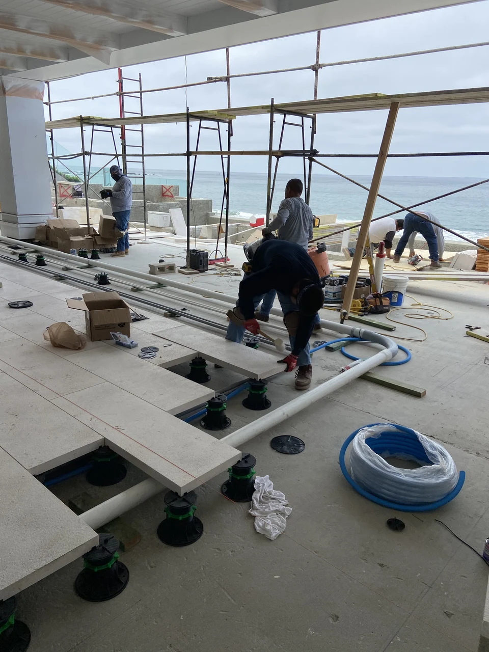 Installers laying terrace pavers on pedestals around visible pipe runs