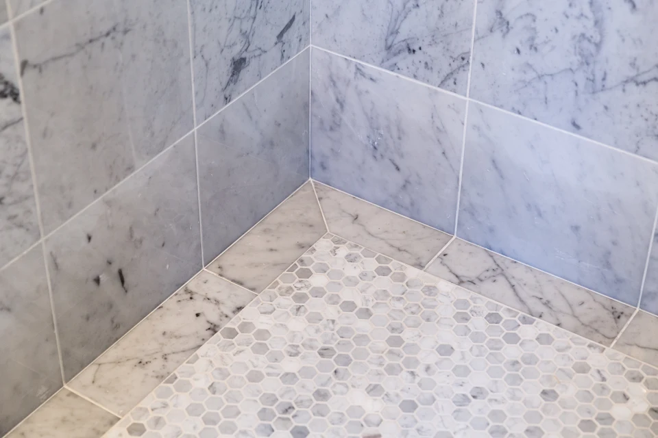 Shower floor mosaic meeting larger veined wall tiles