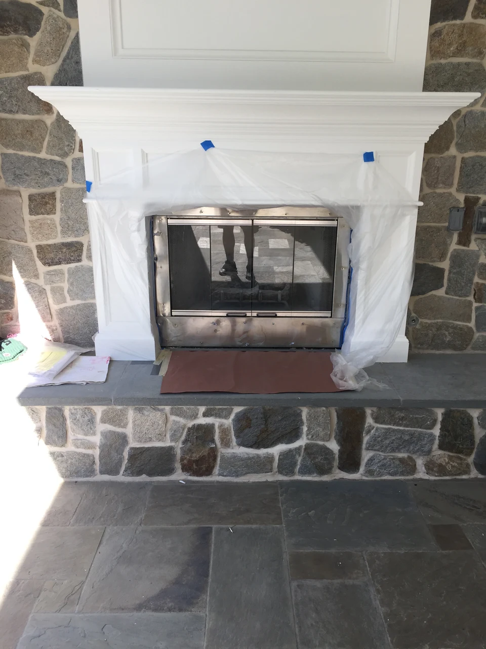 Fireplace during installation with protective wrapping, tape, stone facing and a gray hearth