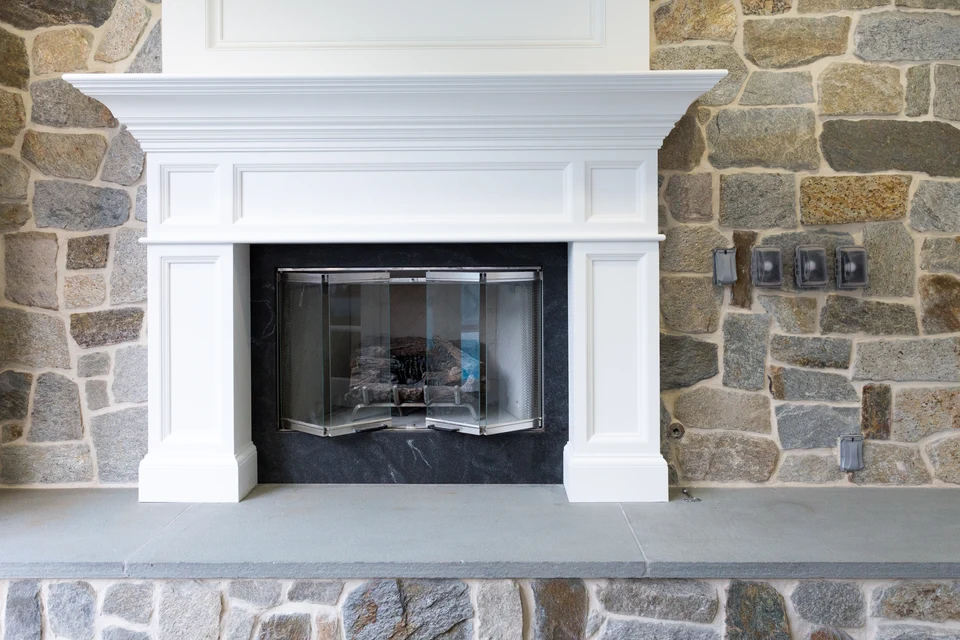White fireplace mantel and paneled surround set into a stone wall above a broad gray hearth