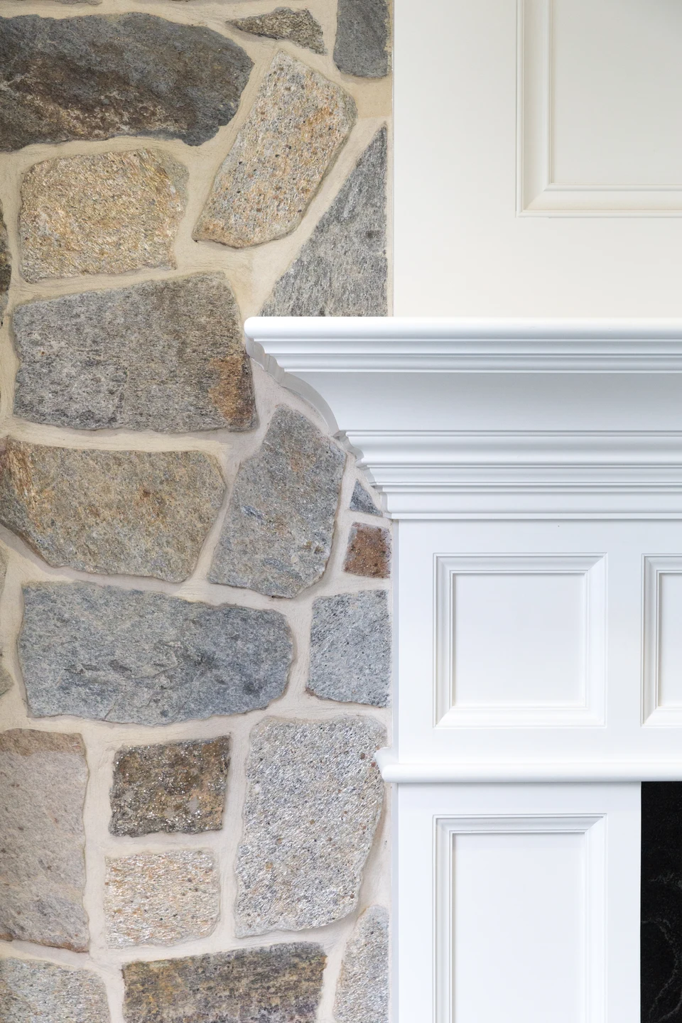 Close-up of stone facing meeting the white profile and paneling of a fireplace mantel