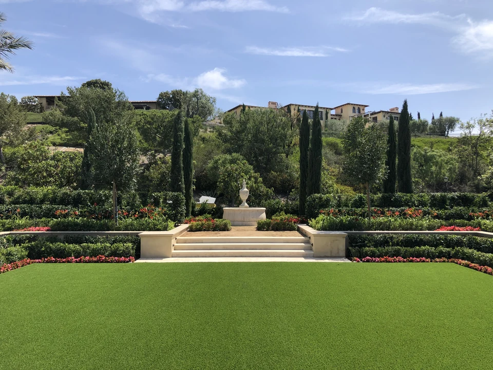 Wide view of artificial lawn, flower borders, stone steps and a garden sculpture