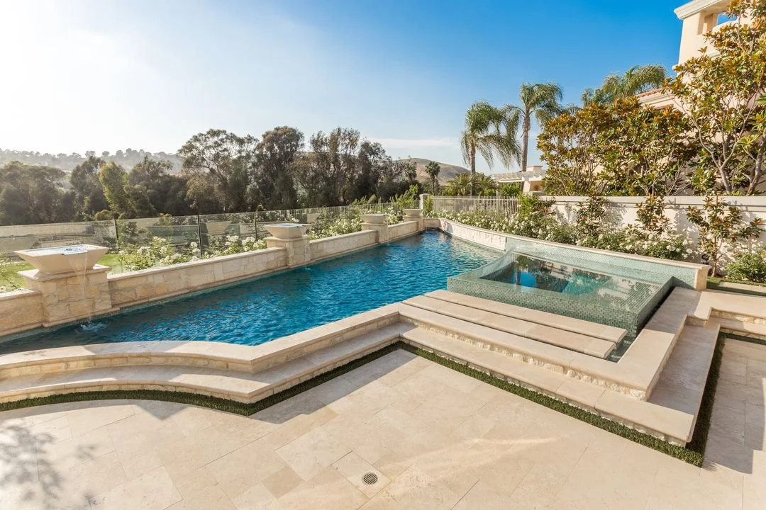 Swimming pool and raised spa framed by pale paving and stone walls