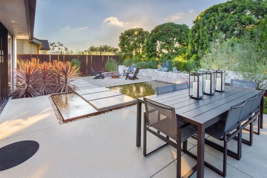 Outdoor dining table beside broad paving and planted borders