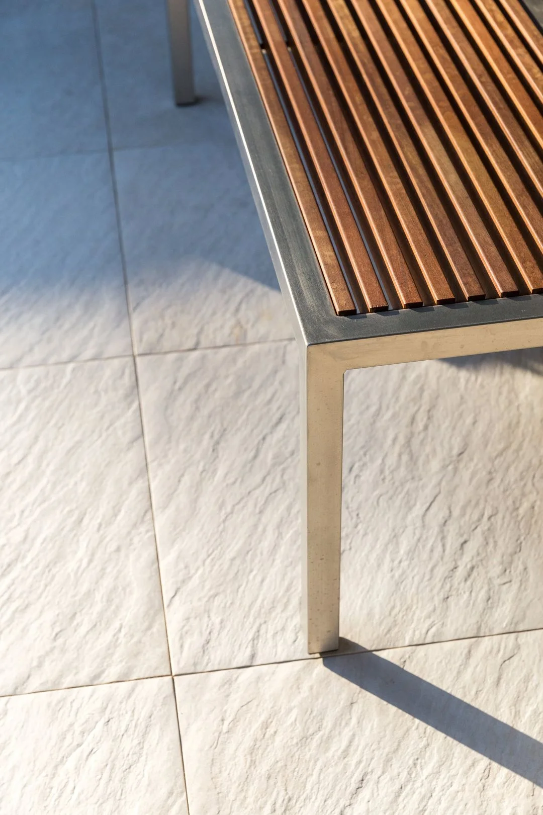 Close view of pale textured paving beside a timber bench