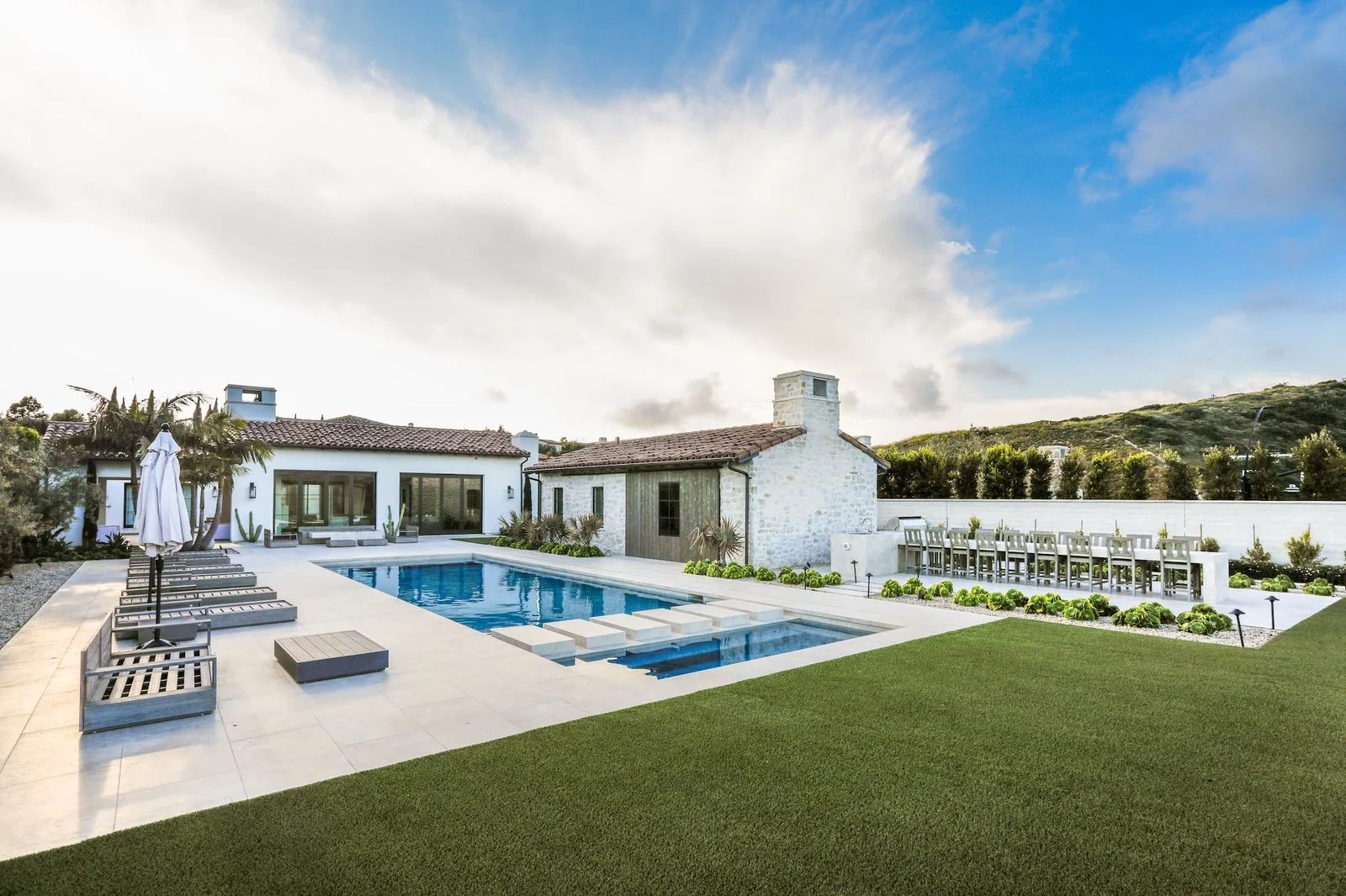 Poolside terrace, lawn and outdoor fireplace beside a white Crystal Cove home