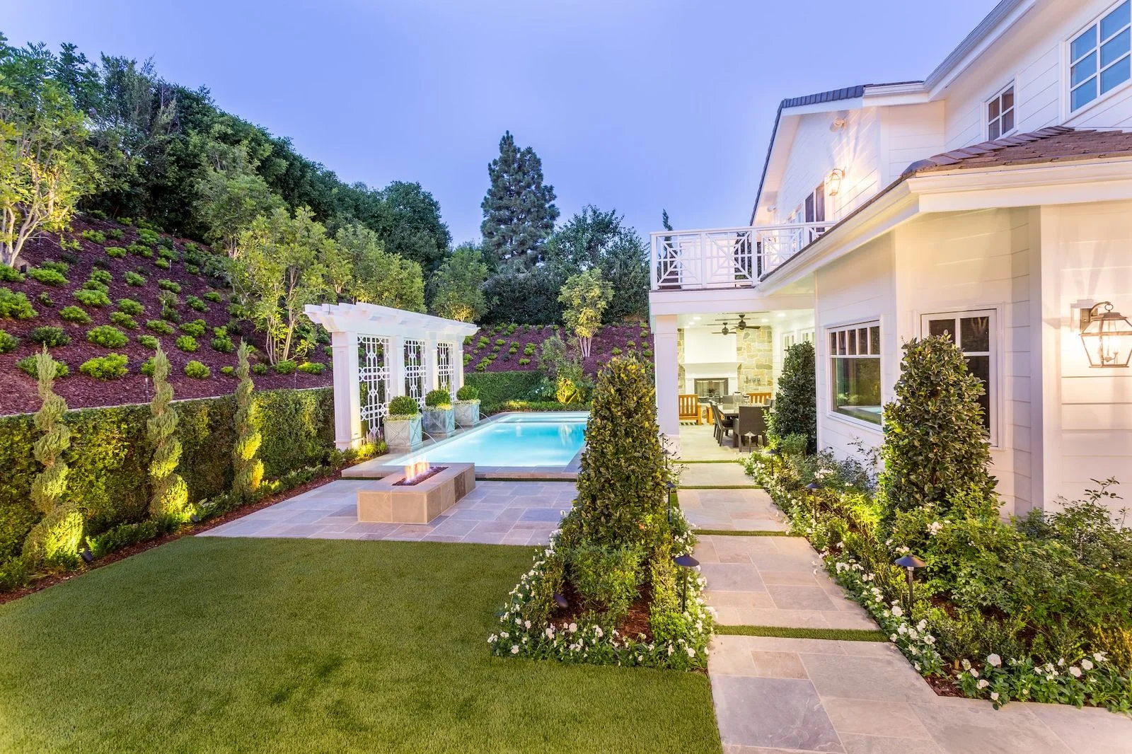 Garden lawn and path beside formal planting, a pool and a light-colored home