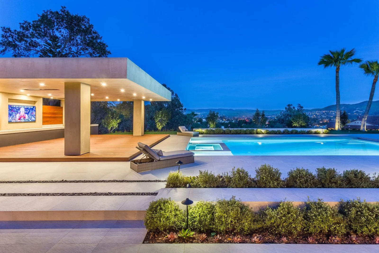 Illuminated poolside pavilion, swimming pool and planted garden at dusk