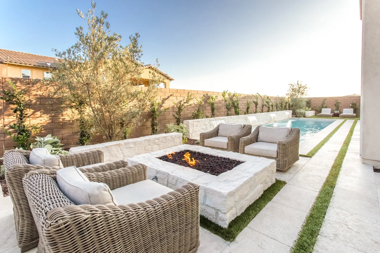 Outdoor sofas around a pale stone fire pit beside lawn-jointed paving and a pool