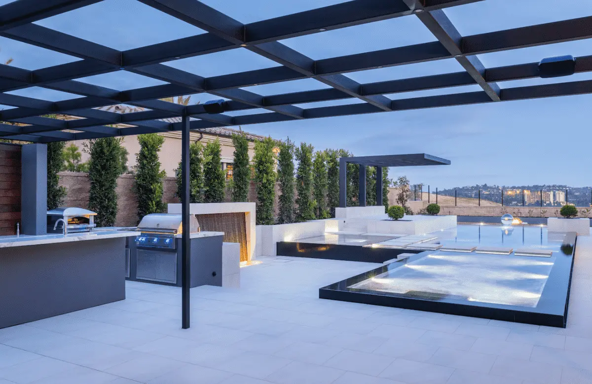 Geometric pool and raised spa beside a covered outdoor kitchen and pale paving