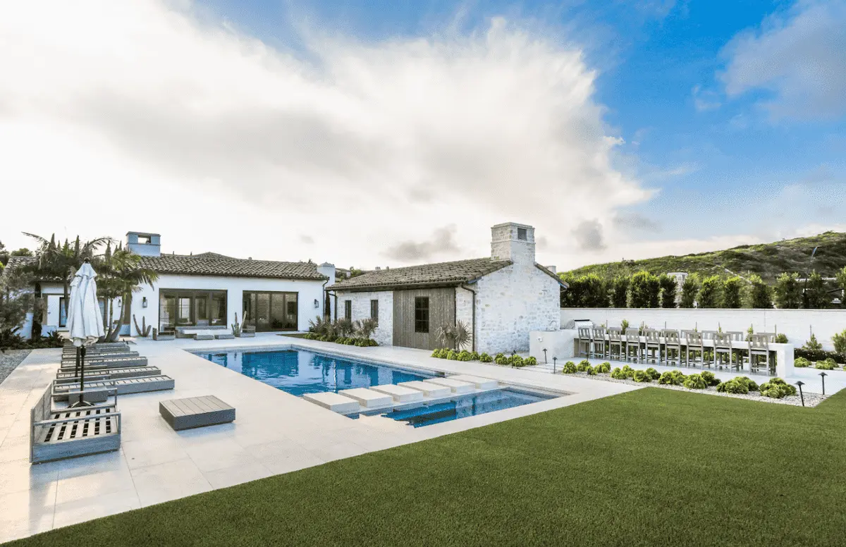 Poolside terrace, lawn and outdoor fireplace beside a white Crystal Cove home