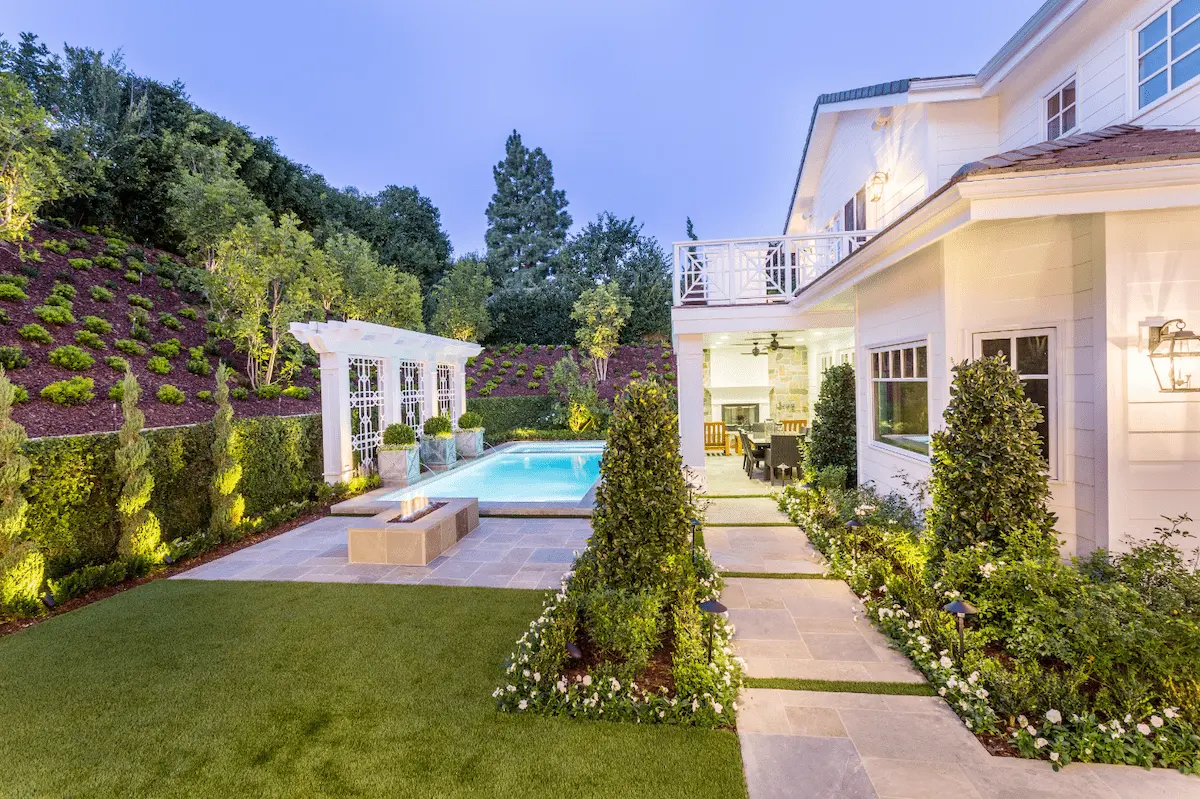 Garden lawn and path beside formal planting, a pool and a light-colored home