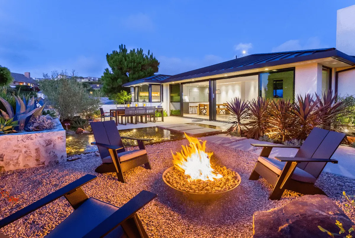 Contemporary fire-pit seating area with sculptural plants beside an illuminated home