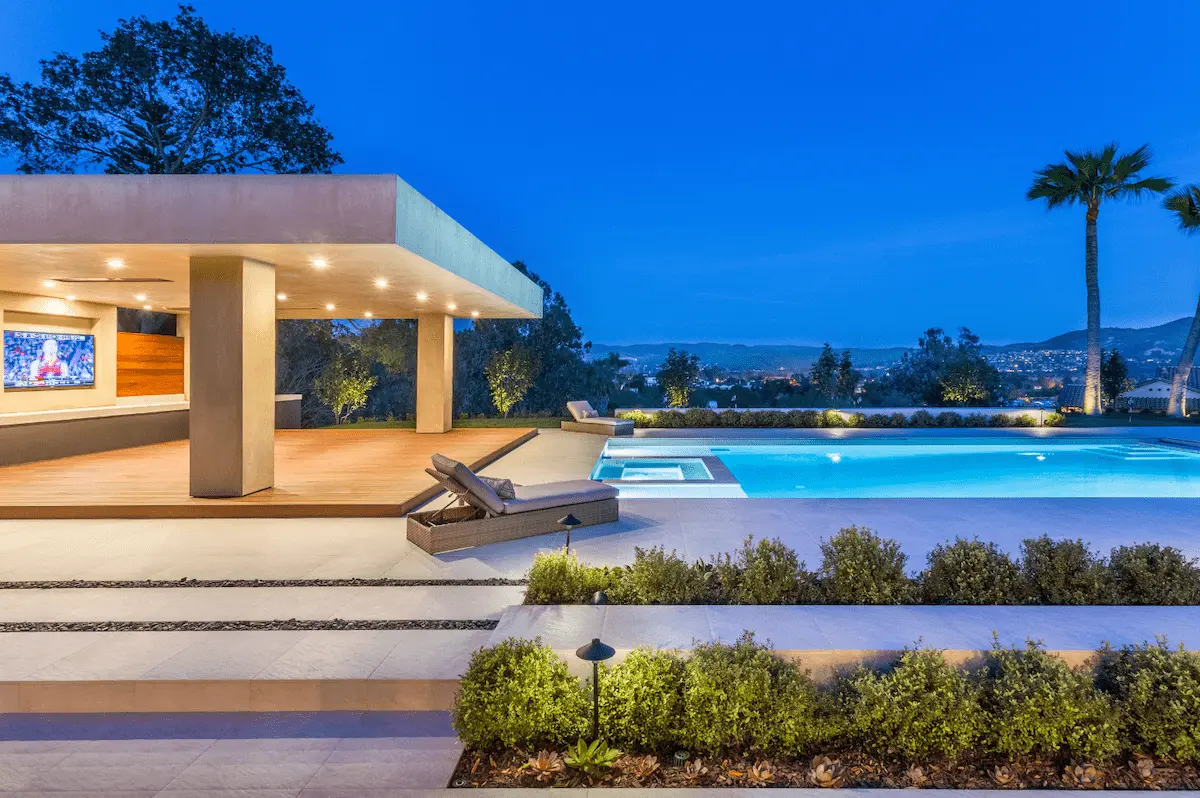 Illuminated poolside pavilion, swimming pool and planted garden at dusk