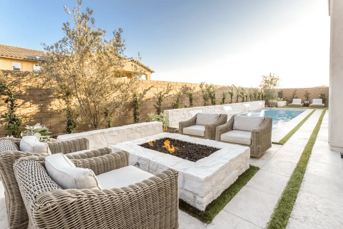 Outdoor sofas around a pale stone fire pit beside lawn-jointed paving and a pool